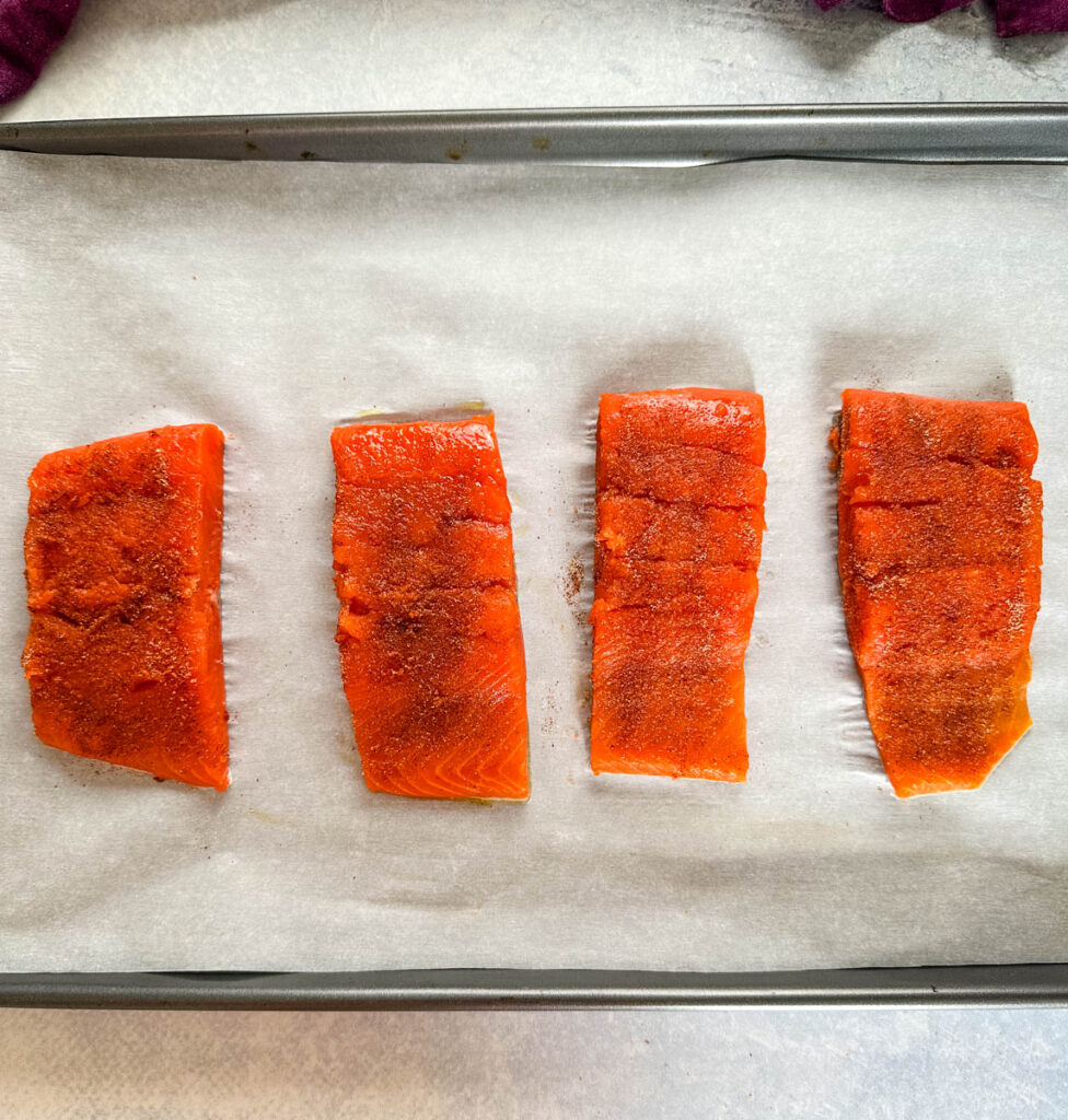 raw seasoned salmon on a sheet pan with parchment paper