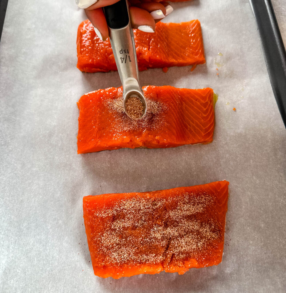 raw seasoned salmon on a sheet pan with parchment paper