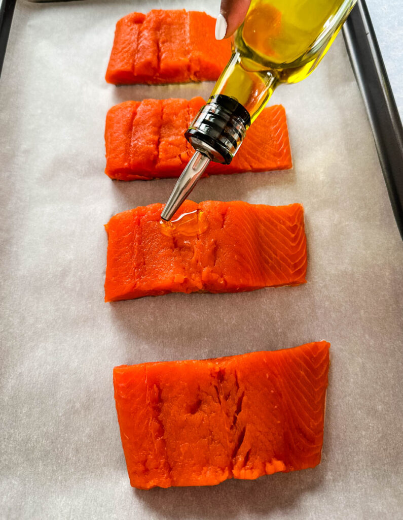 raw salmon drizzled with olive oil on a sheet pan with parchment paper