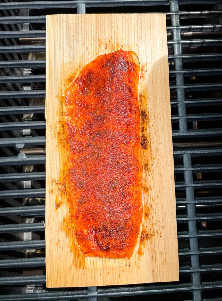 raw salmon on a cedar plank rubbed with spices and brown sugar and on a grill