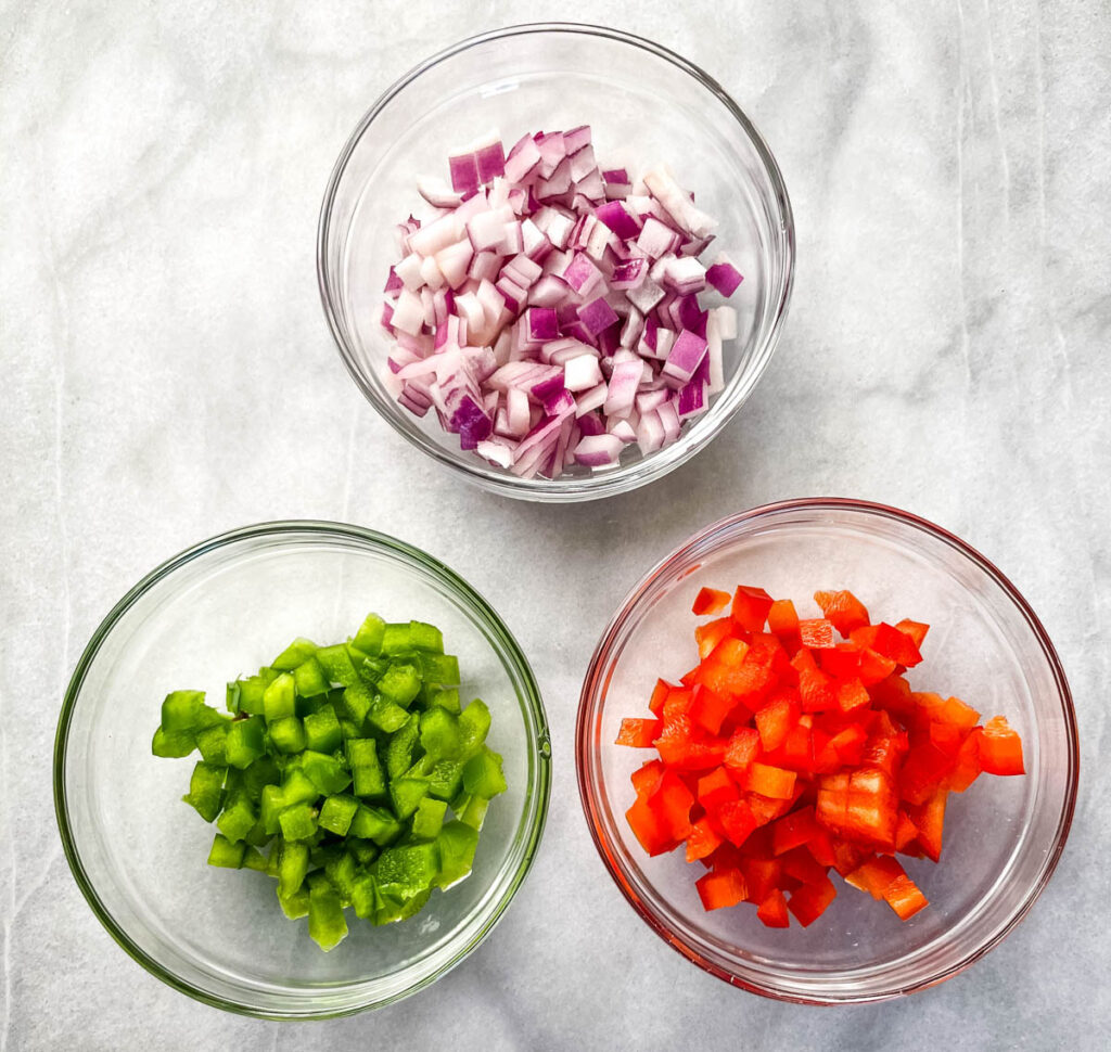 chopped onions, green peppers, and red peppers in separate glass bowls
