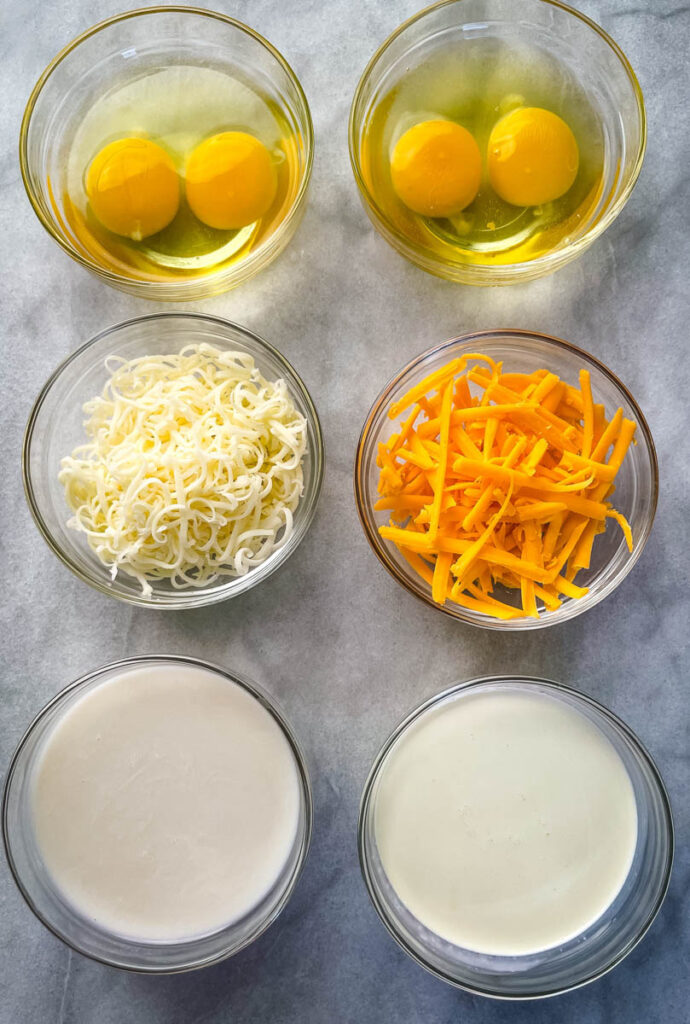 eggs, shredded cheese, heavy cream, and milk in separate glass bowls