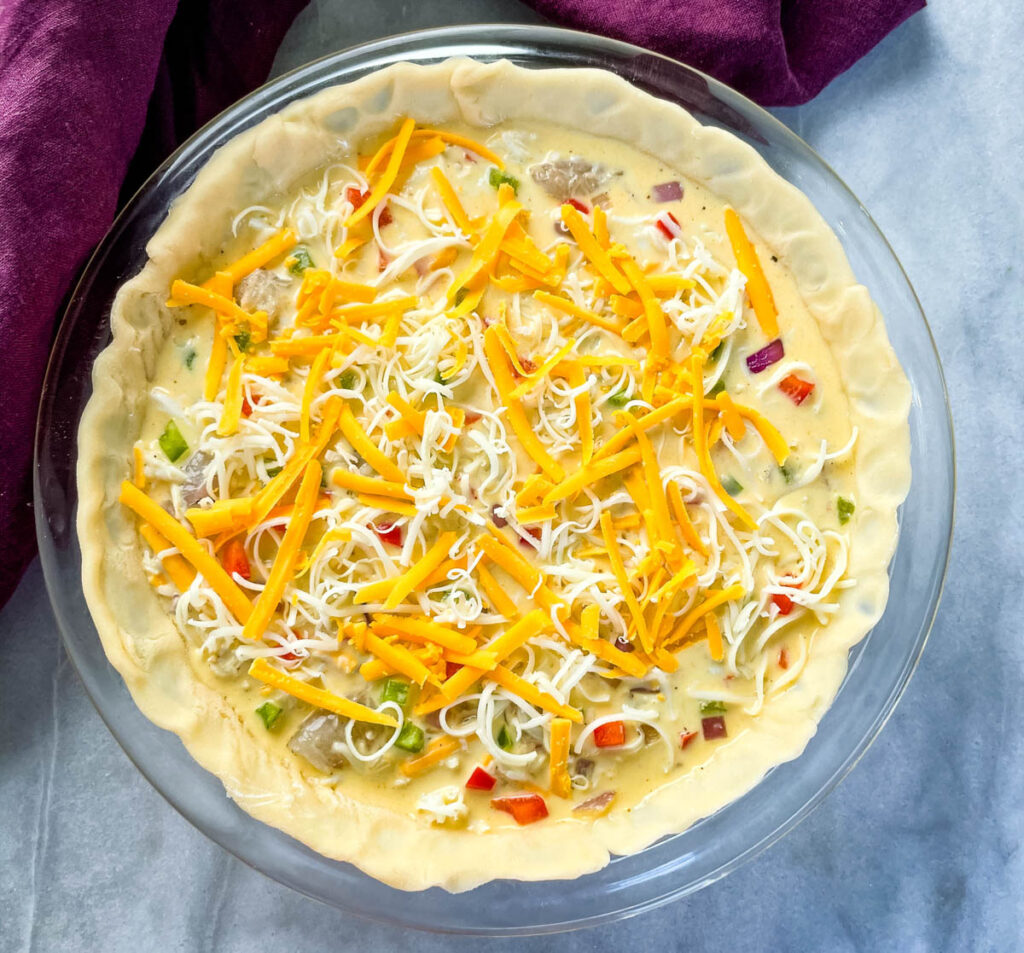 unbaked crab quiche with cheese in a glass pie plate