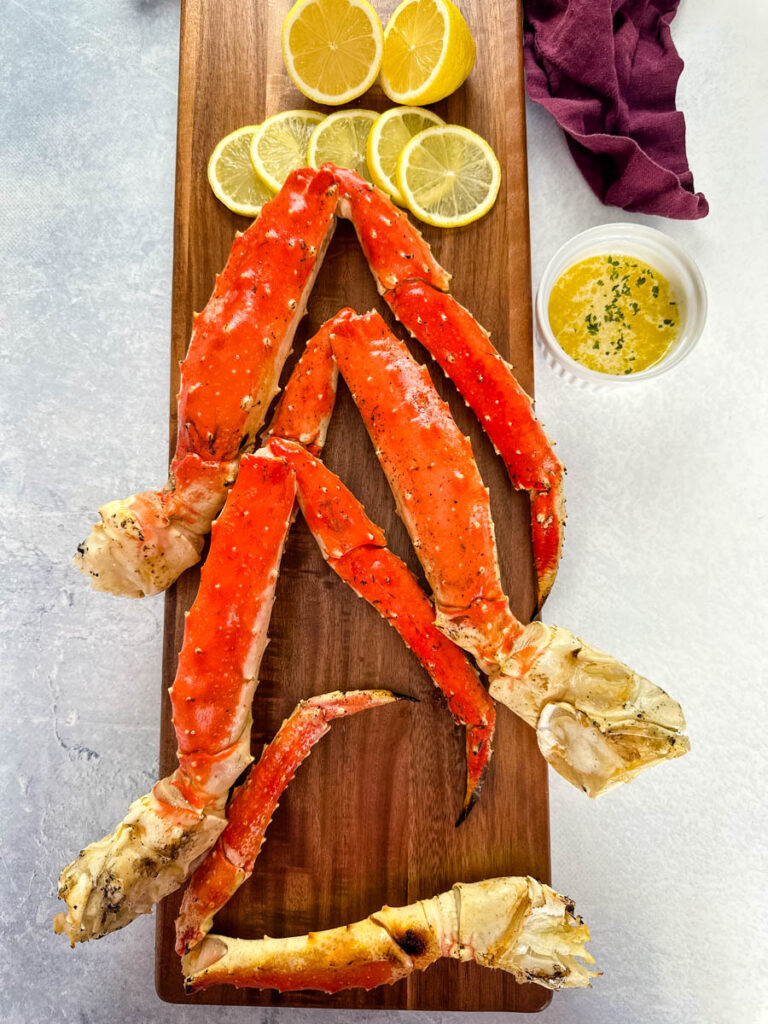 grilled crab legs on a wooden board with fresh lemon and garlic butter