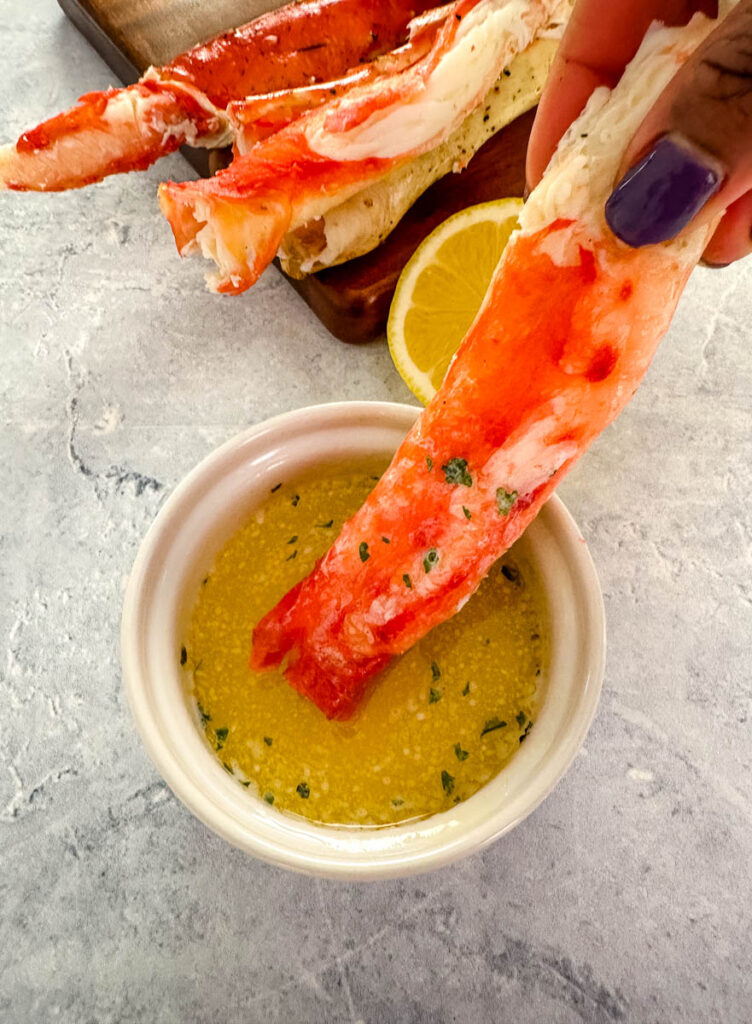 person holding cracked king crab leg in melted butter