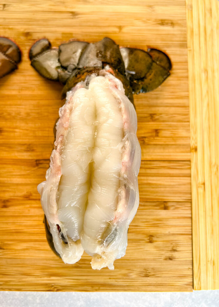 butterflied cold water lobster tail on a wooden cutting board