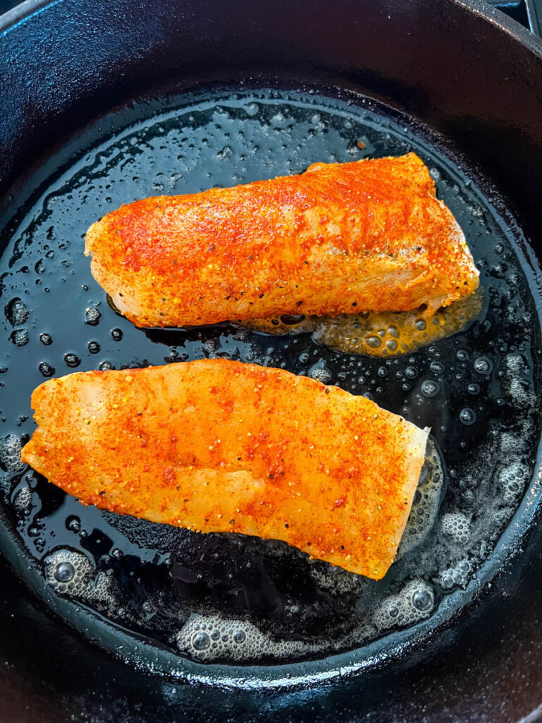 seasoned cod fillets in a cast iron skillet with butter