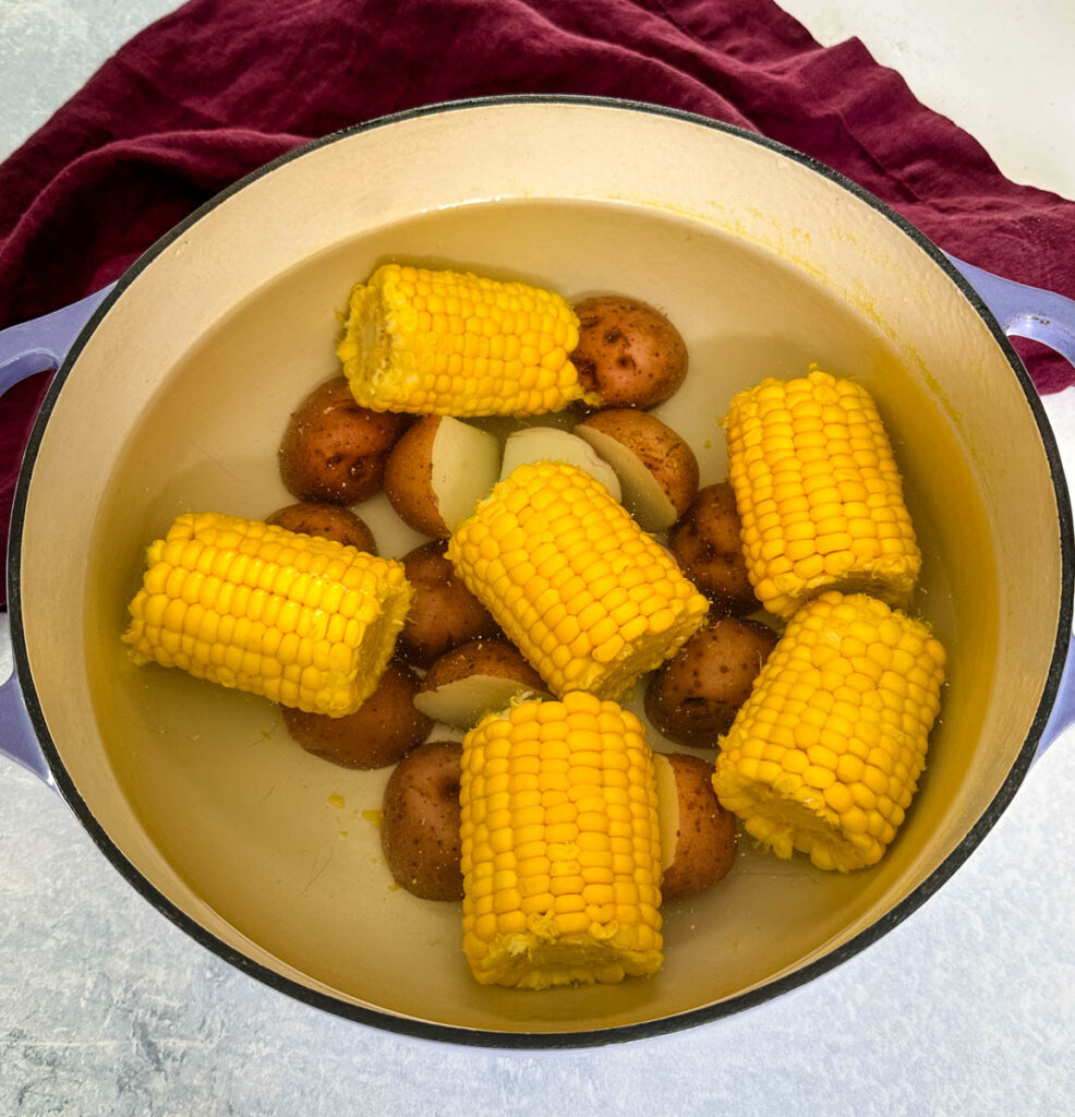 fresh corn on the cob and sliced red potatoes with water in a Dutch oven