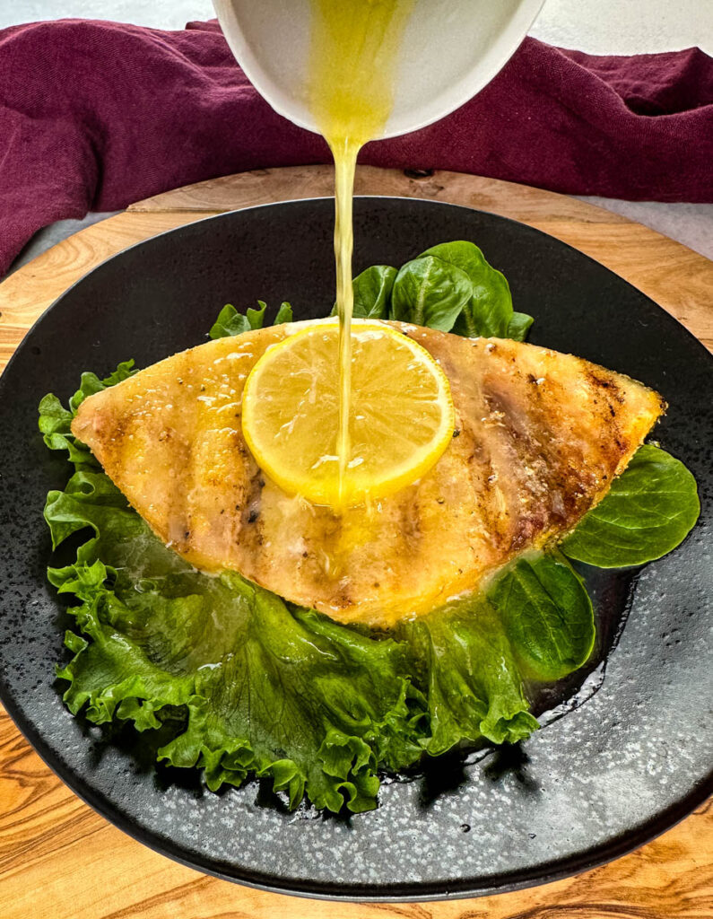 smoked swordfish with lemon and greens on a black plate drizzled with lemon butter