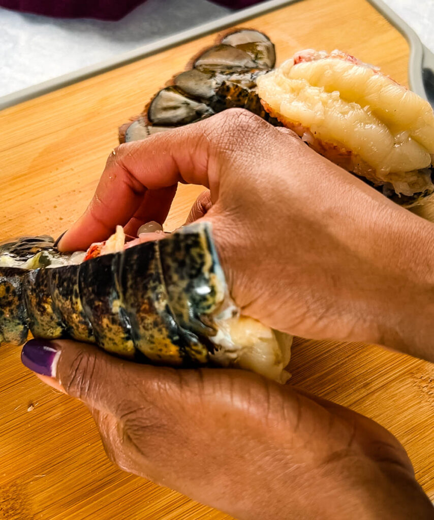 person pulling meat out of raw lobster tail