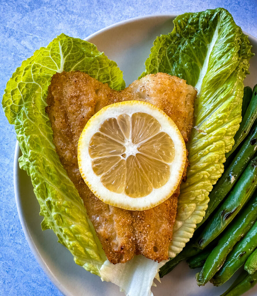 air fryer cod fish on a plate with fresh lemon and lettuce