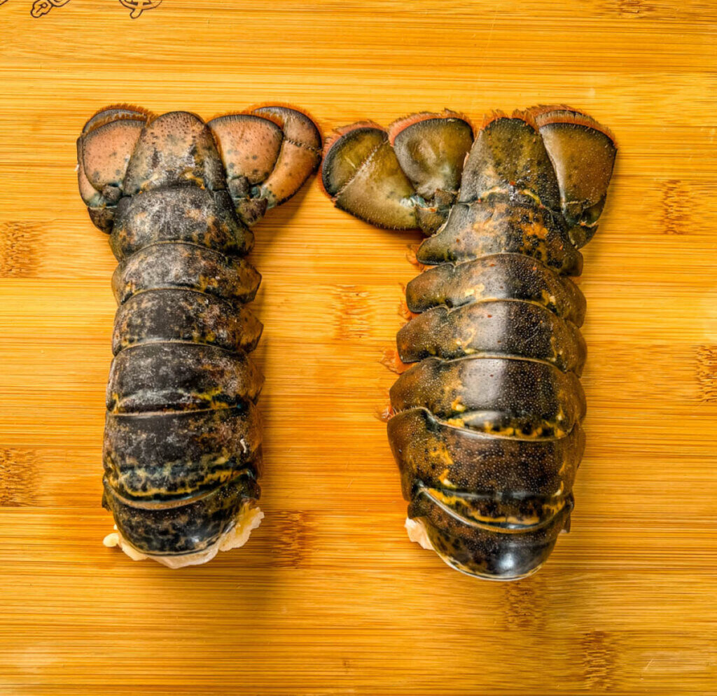 2 raw lobster tails on a cutting board