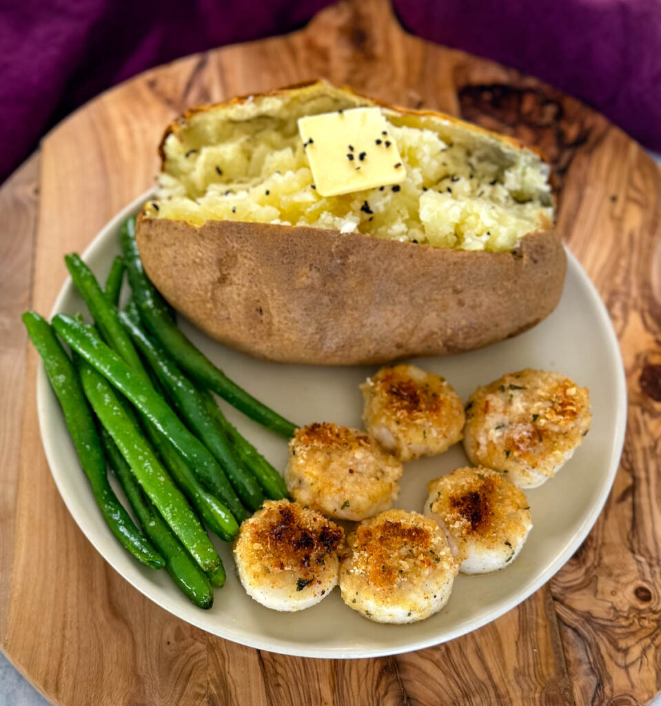 oven baked scallops topped with breadcrumbs and lemon wine butter sauce on a plate with a baked potato and green beans