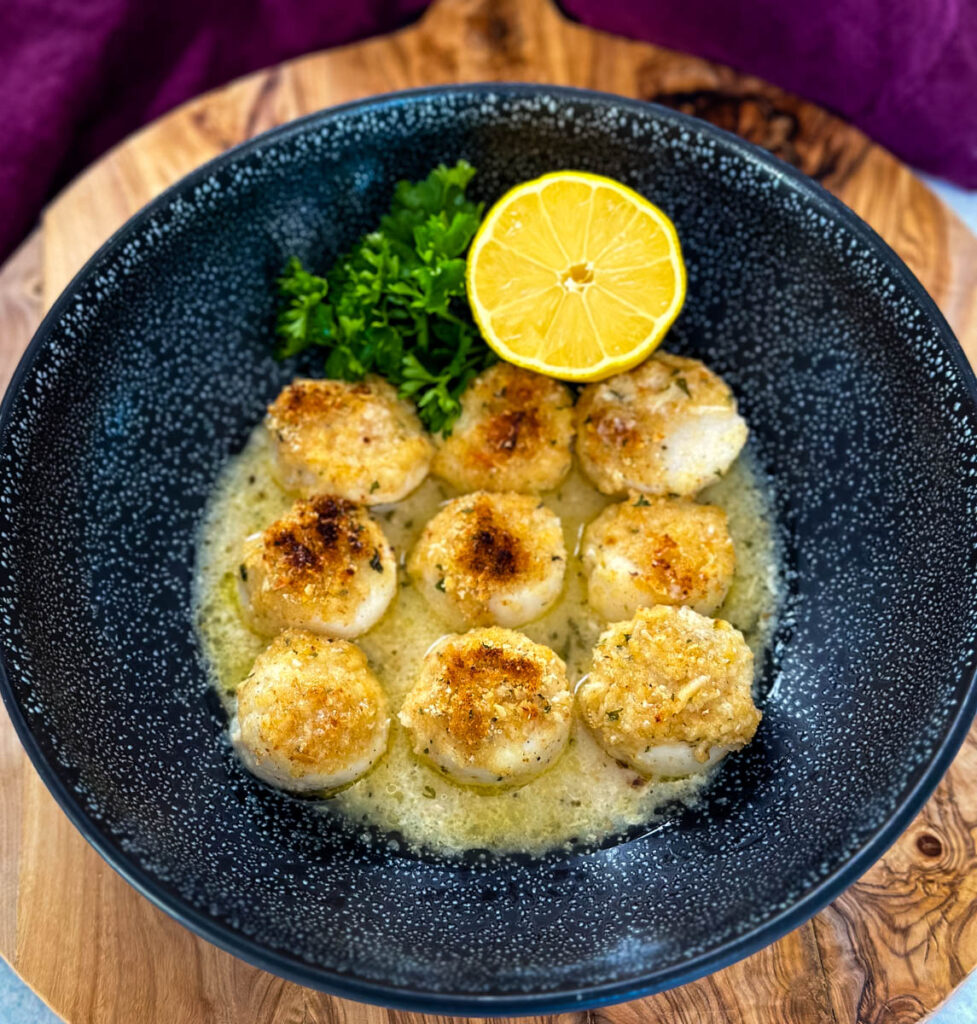 oven baked scallops topped with breadcrumbs and lemon wine butter sauce in a black bowl with fresh lemon
