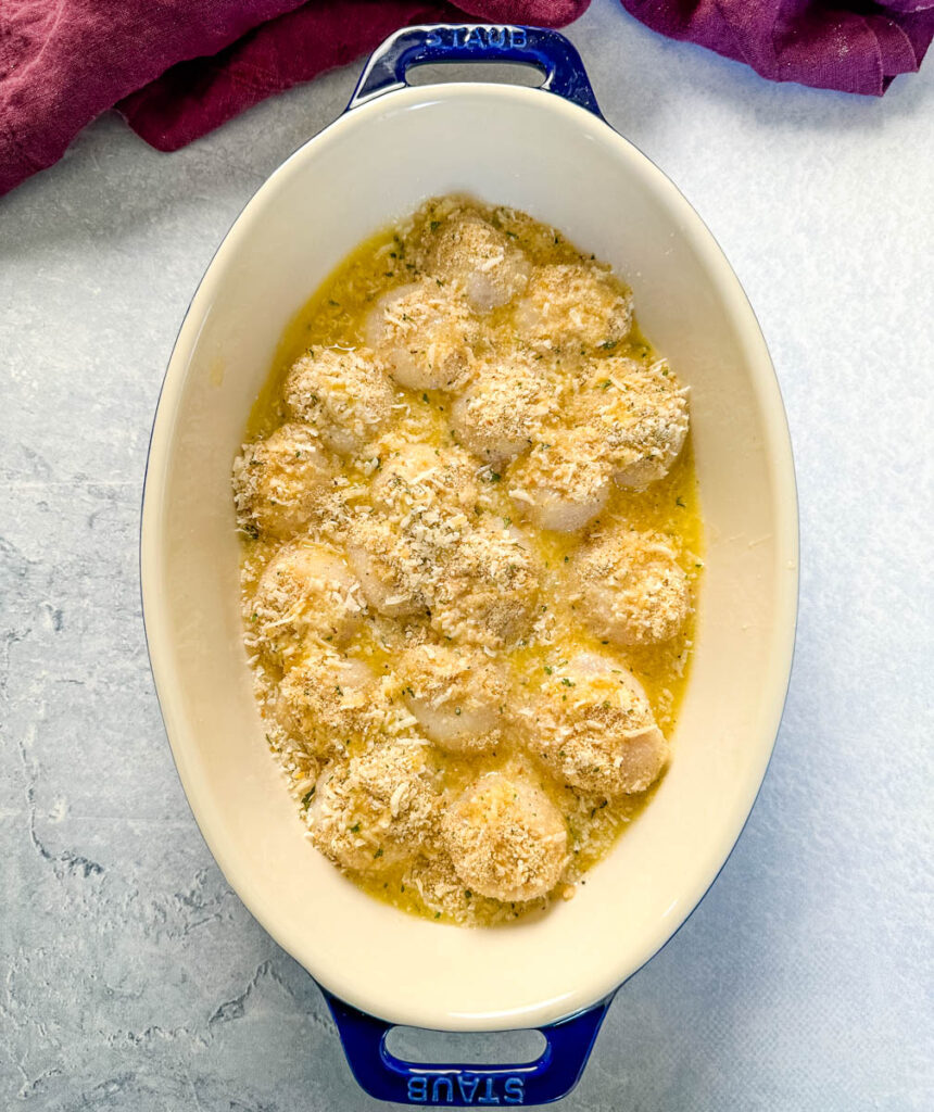 raw scallops topped with spices, wine sauce, and breadcrumbs in a baking dish