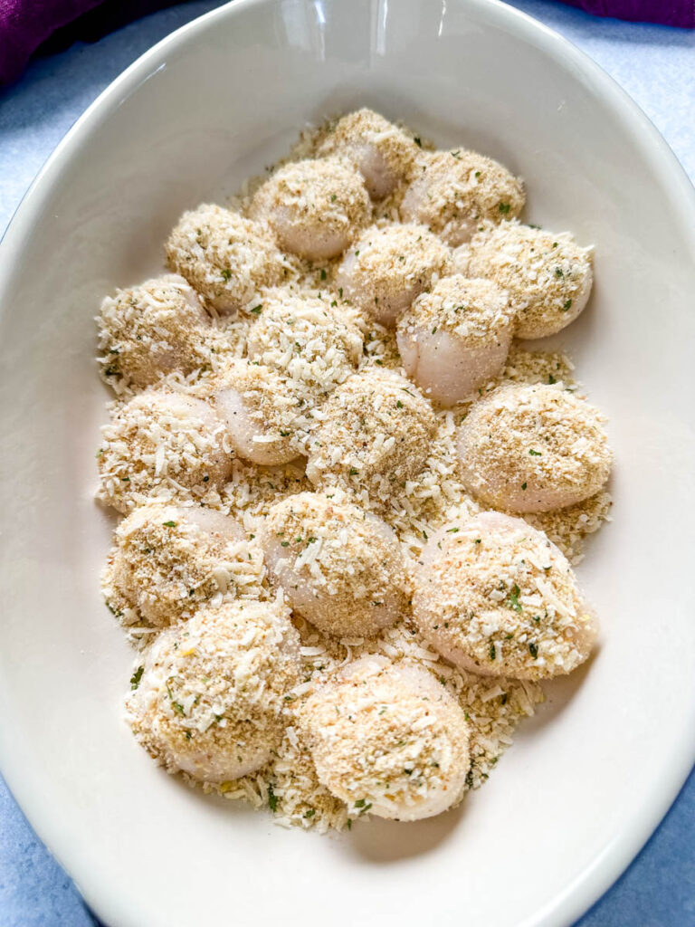 raw scallops topped with spices and breadcrumbs in a baking dish
