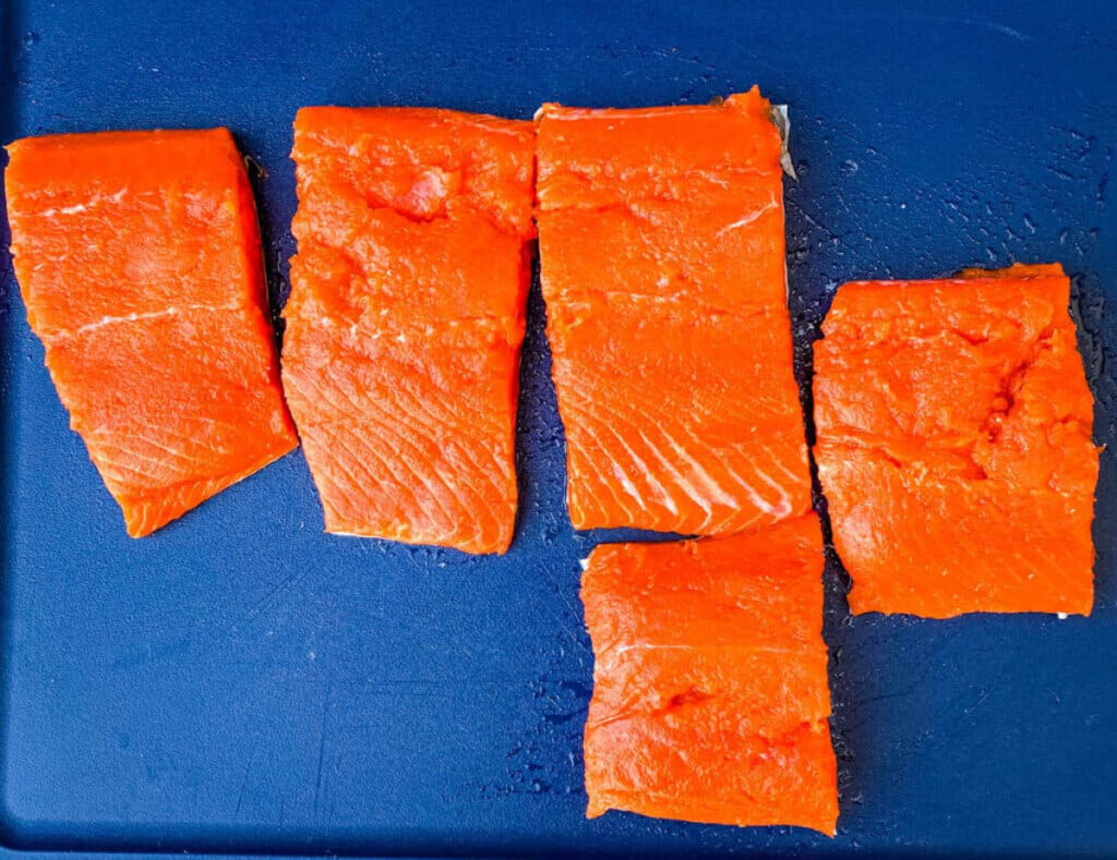 raw salmon sliced into portions on a cutting board
