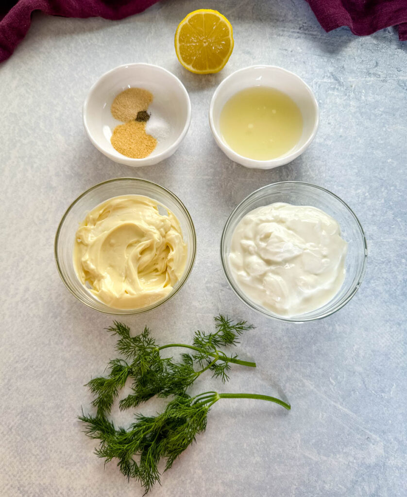 fresh lemon juice, spices, mayo, Greek yogurt, and fresh dill on a flat surface