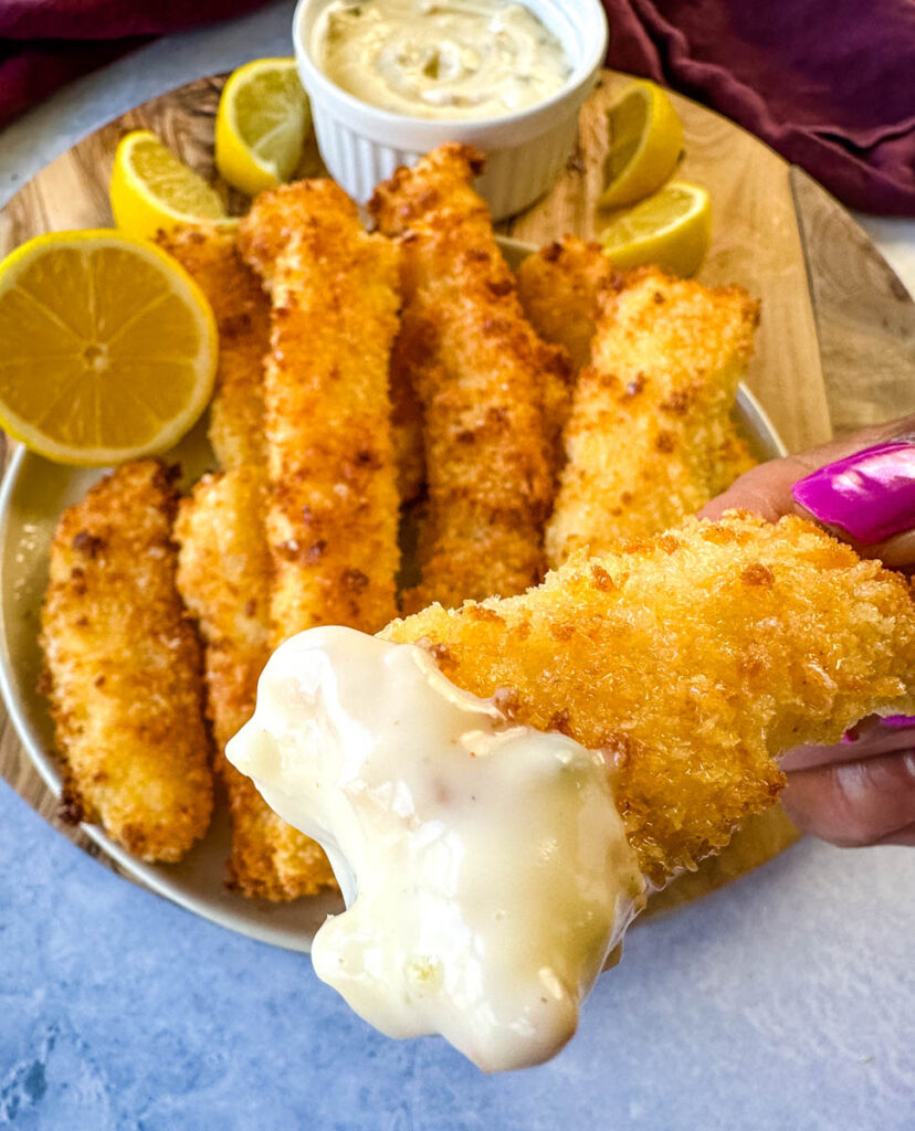person holding homemade fish sticks dipped in tartar sauce