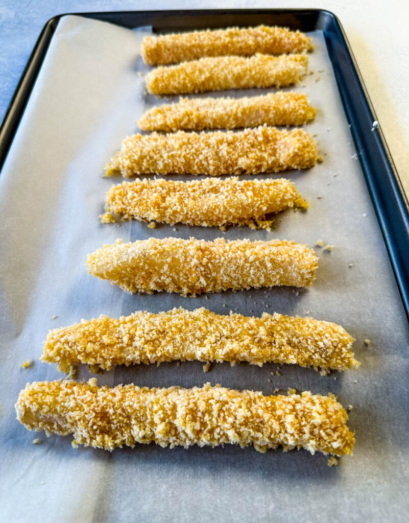 unbaked breaded homemade fish sticks on a parchment paper lined sheet pan
