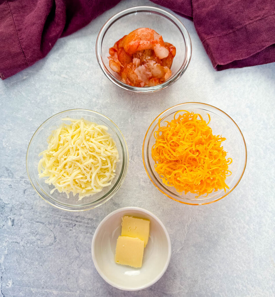 raw lobster, butter, and shredded cheese in separate glass bowls