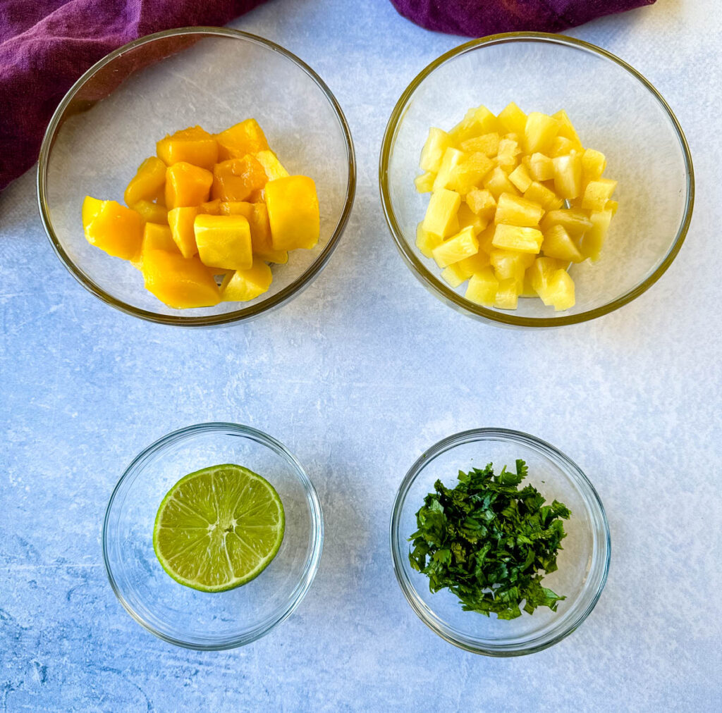 mango, pineapples, lime, and cilantro in separate glass bowls