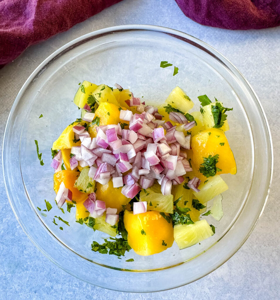 mango pineapple salsa with onion and cilantro in a glass bowl