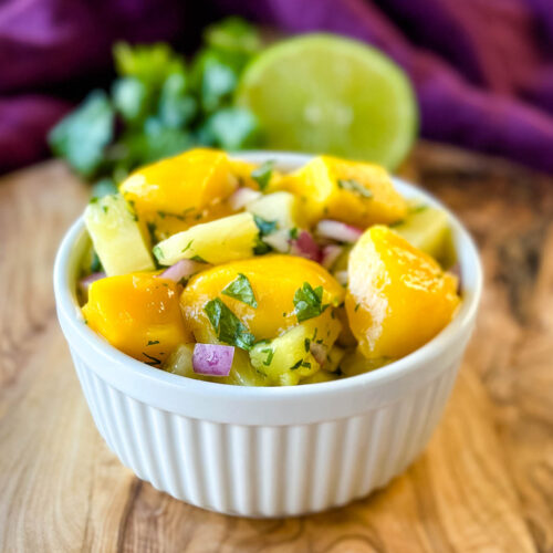 mango pineapple salsa with onion and cilantro in a white bowl