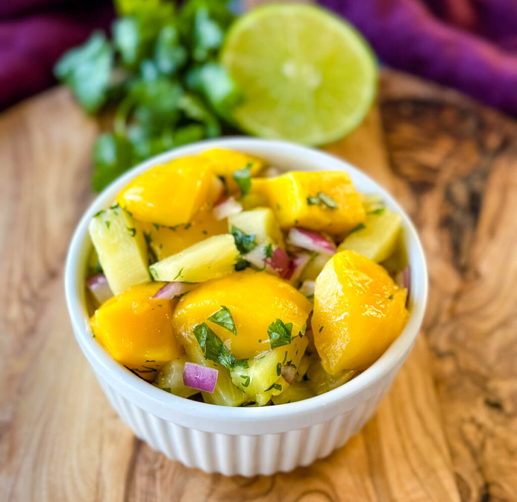 mango pineapple salsa with onion and cilantro in a white bowl