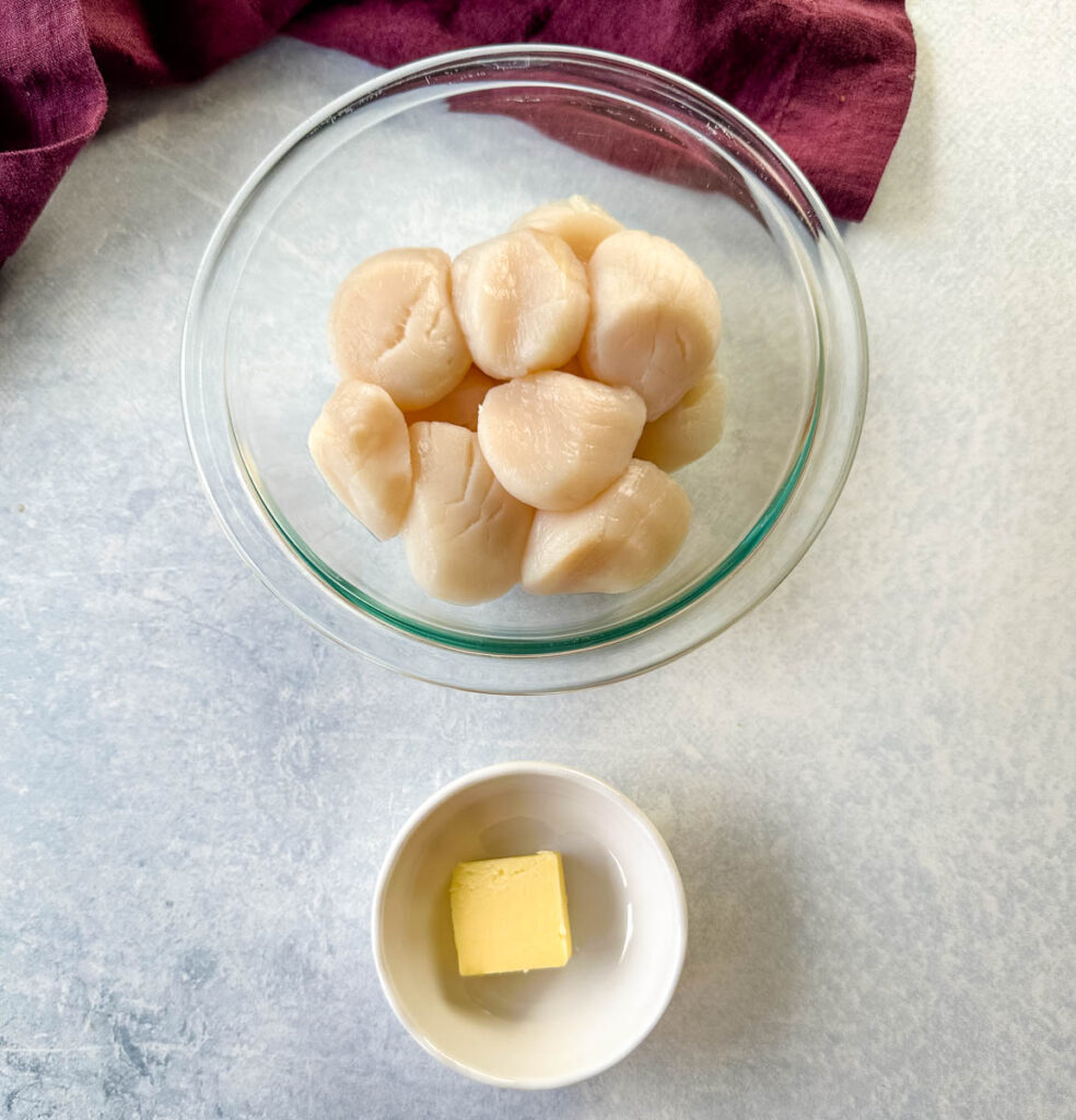 raw scallops in a glass bowl and butter in a white bowl