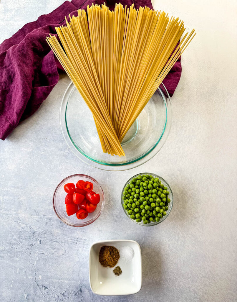 dry spaghetti pasta, tomatoes, peas, and spices in separate bowls