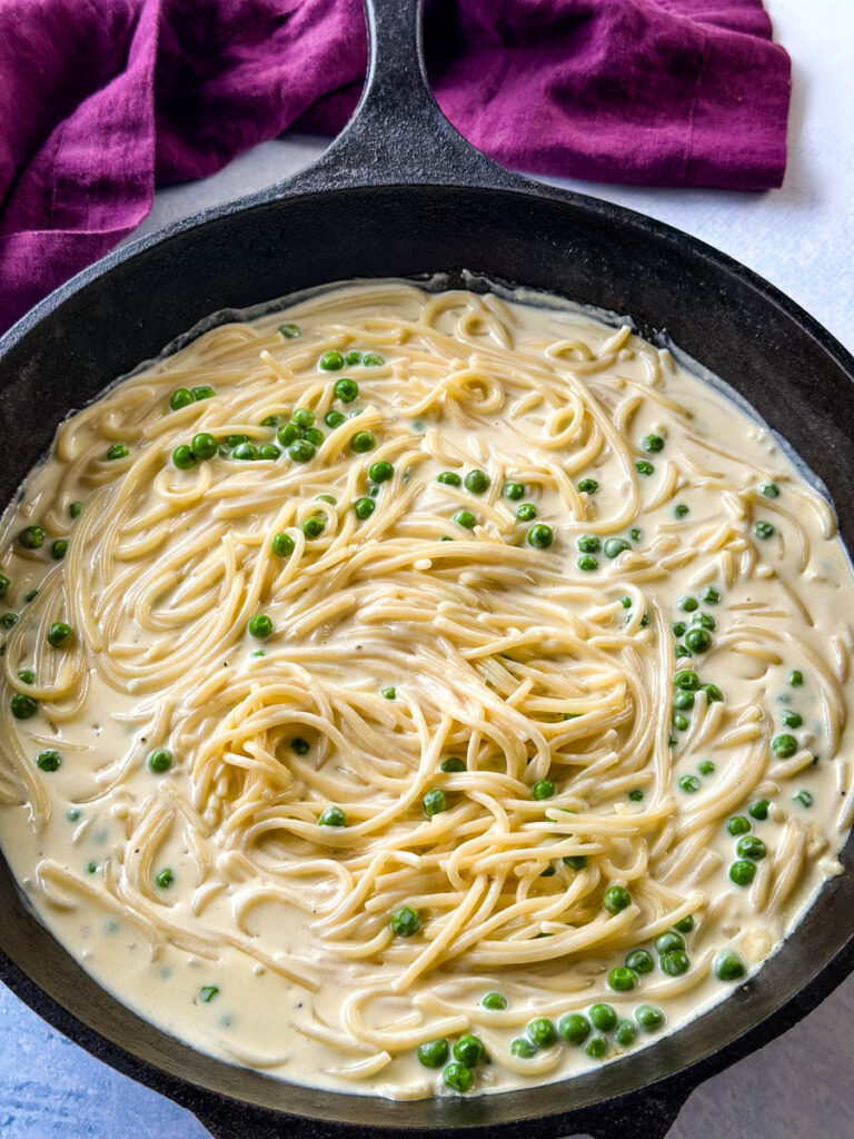 spaghetti and white cream sauce with peas in a cast iron skillet