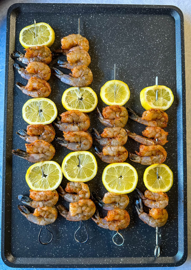 seasoned uncooked shrimp on skewers with lemon on a sheet pan