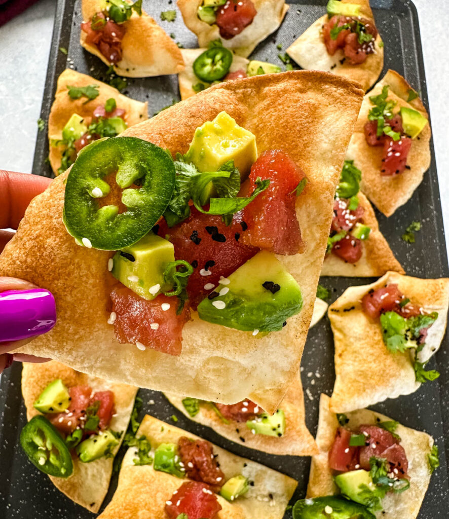 person holding a chip with ahi tuna poke sushi nachos with avocado sesame seeds, jalapenos, and cilantro