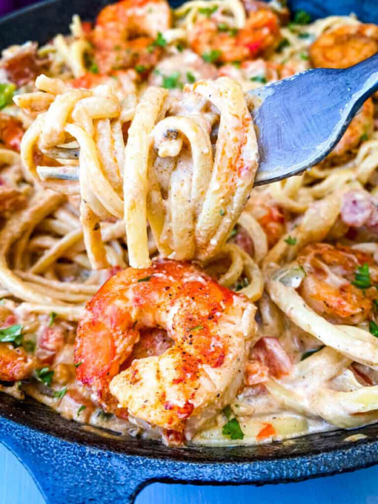 a fork full of Cajun shrimp pasta with linguine, sausage, and cream sauce in a pan