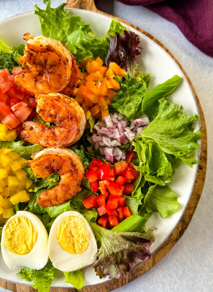 Cajun shrimp salad with hard boiled eggs, bell peppers, and tomatoes on a white plate