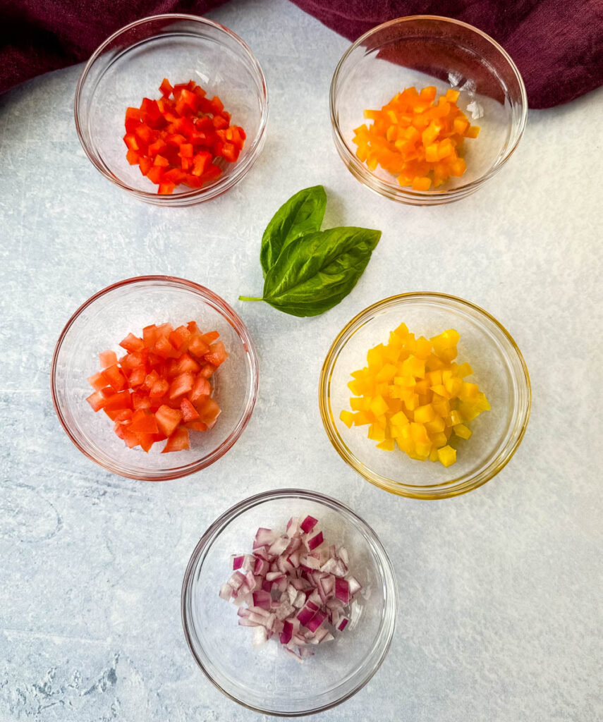 chopped bell peppers, onion, fresh basil, and chopped tomatoes in separate glass bowls