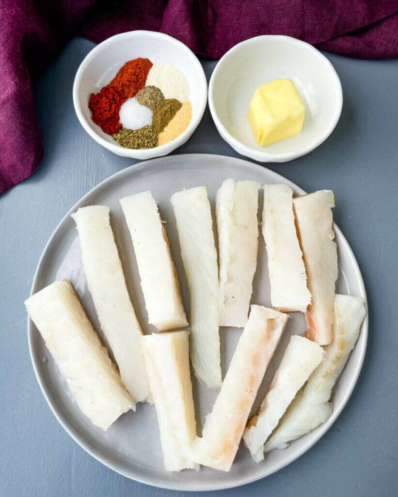 raw slices of cod fish on a plate with spices and butter in separate bowls