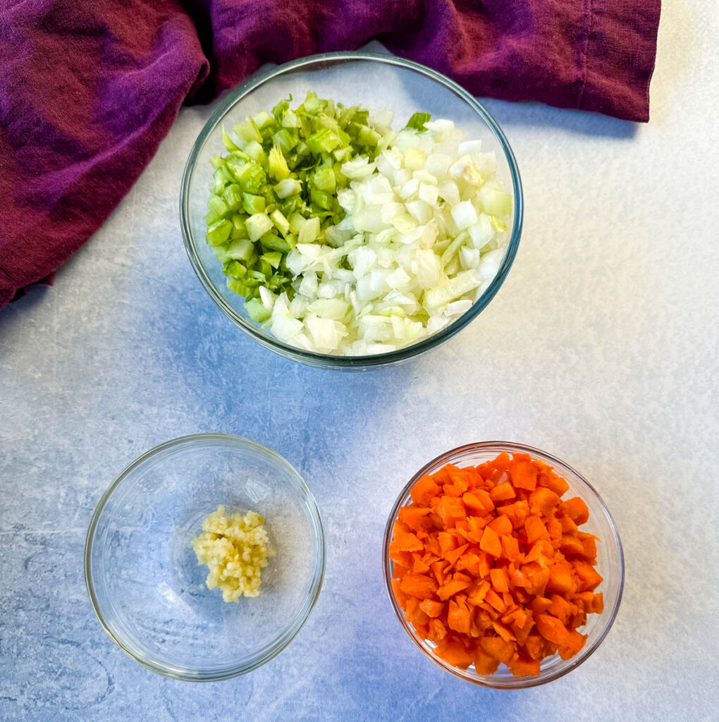 fresh chopped celery, onions, carrots, and garlic in separate glass bowls