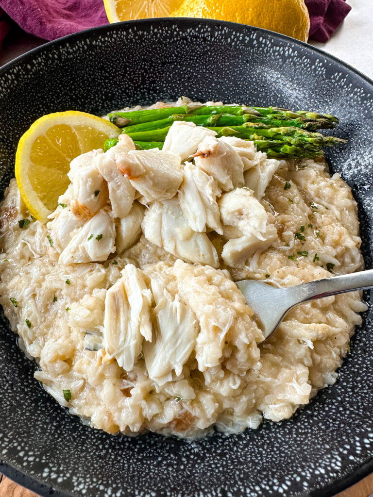 crab risotto in a black bowl with fresh lemon and asparagus