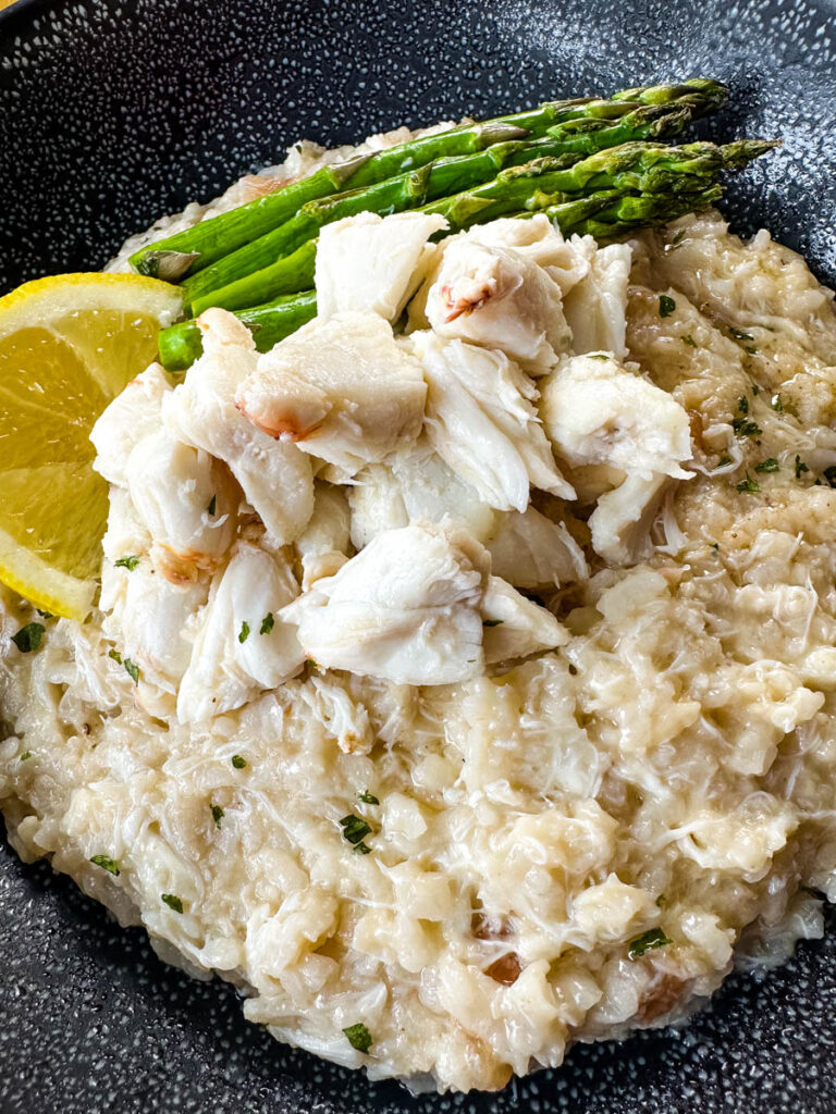 crab risotto in a black bowl with fresh lemon and asparagus