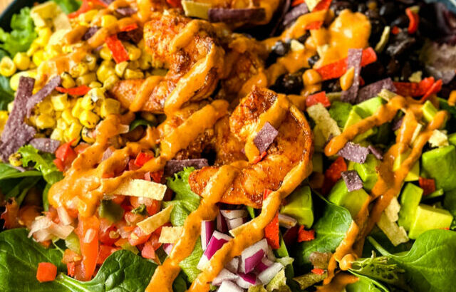 shrimp taco salad with avocado, corn, black beans, onions and salsa on a blue plate with Chipotle ranch dressing