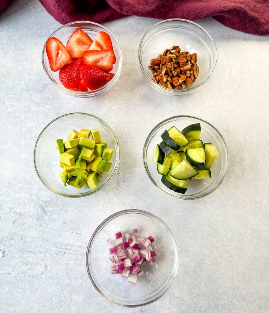 pecans, cucumbers, strawberries, avocado, and onions in separate glass bowls