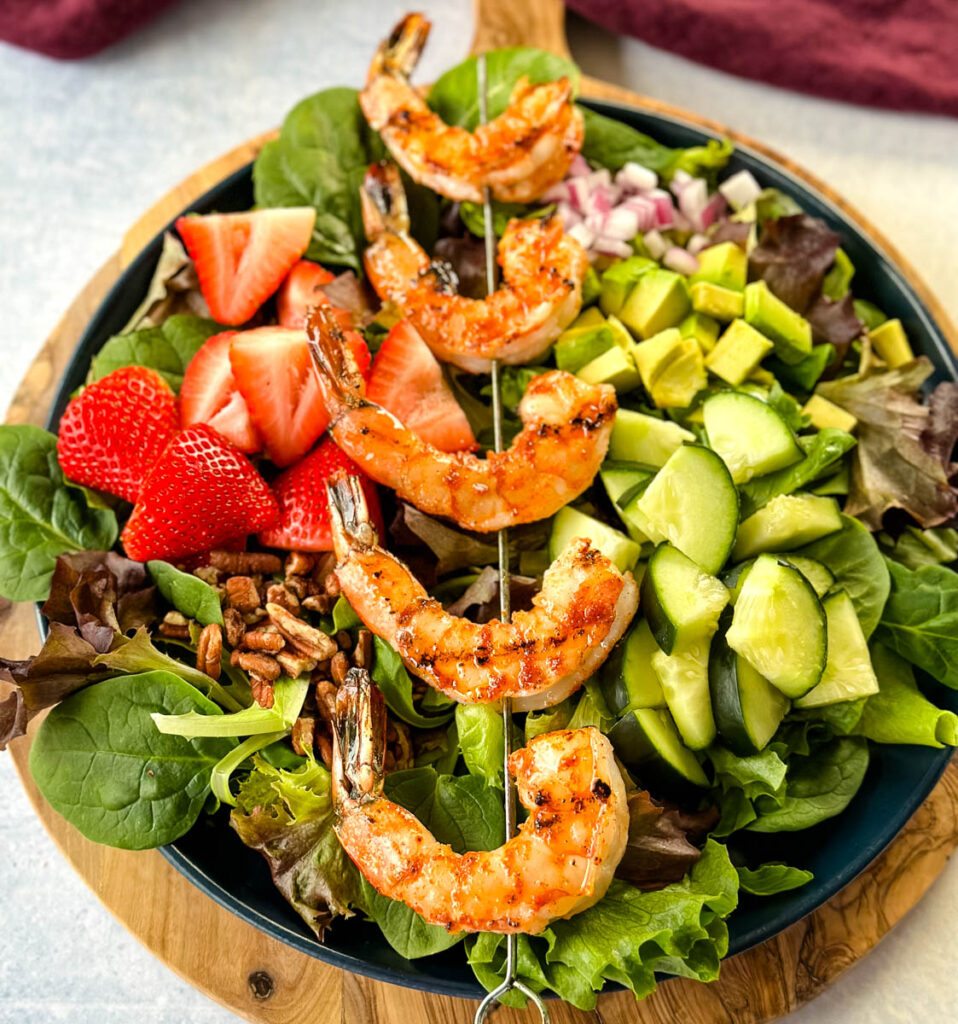 grilled shrimp salad on a plate with mixed greens, strawberries, avocado, and onions