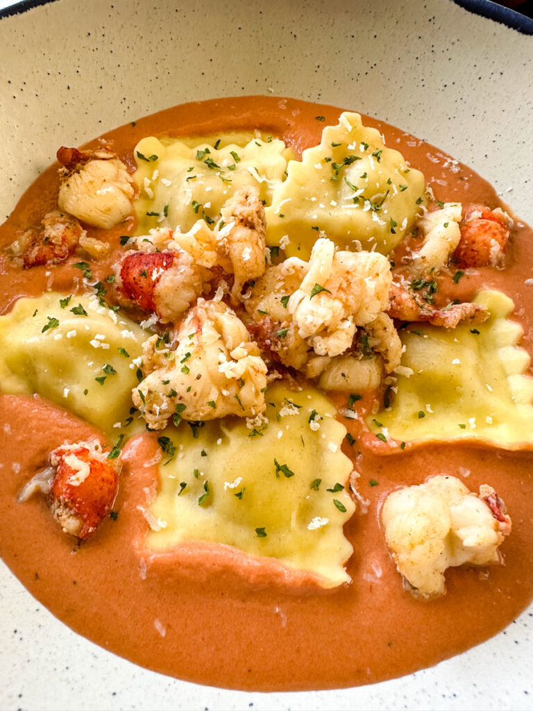 lobster ravioli with chunks of lobster and tomato cream sauce in a white bowl