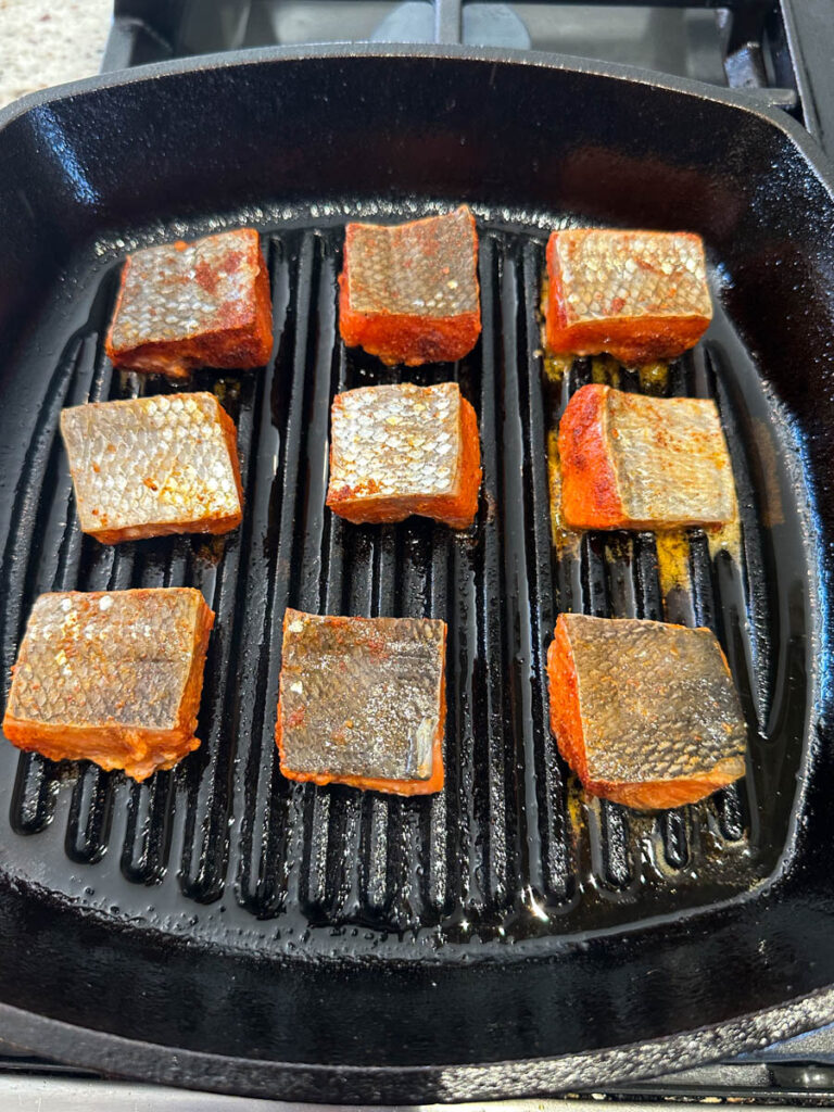 raw sliced salmon bites chunks in a cast iron grill pan