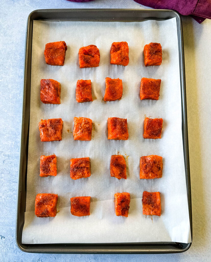 raw sliced salmon bites chunks on a parchment paper lined sheet pan