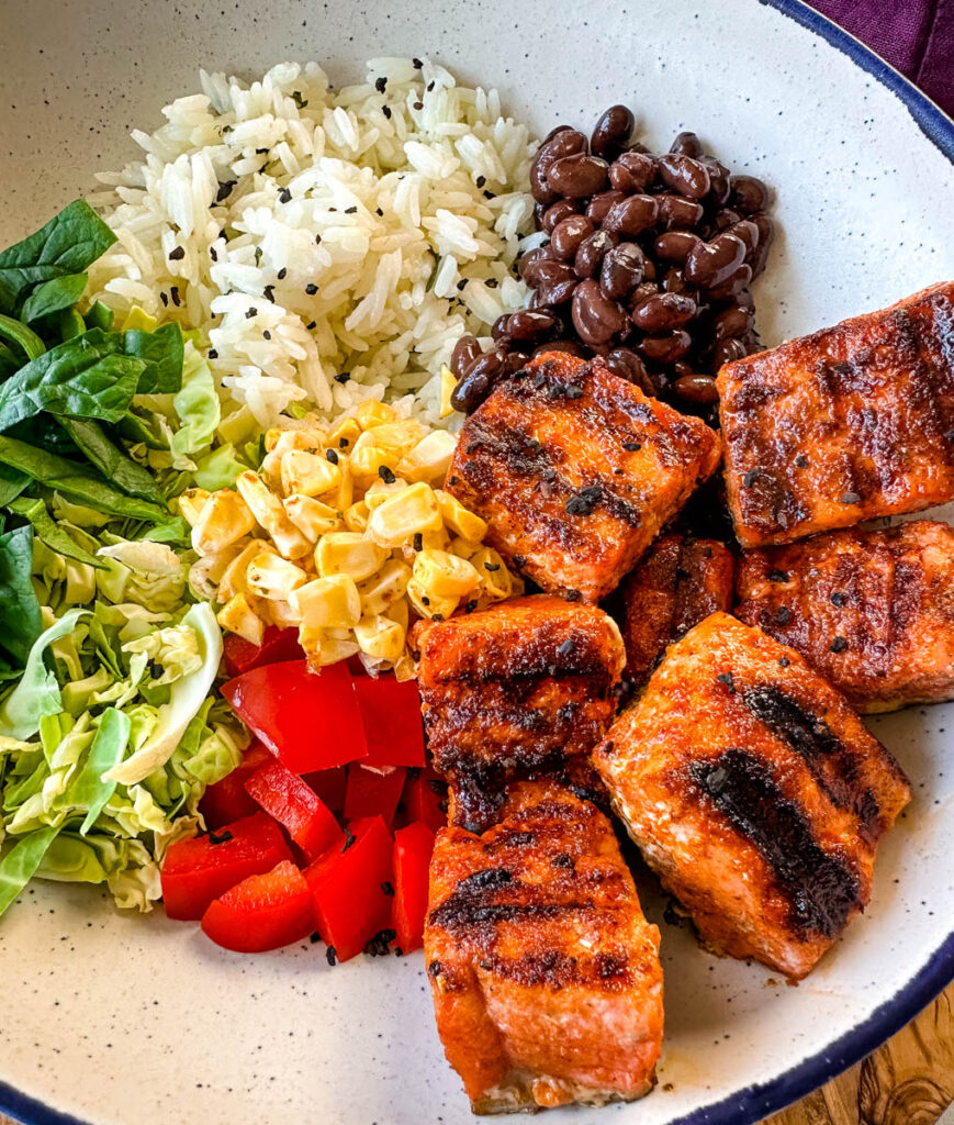 salmon rice bowl with black beans, spinach, shredded brussels sprouts, bell peppers in a white bowl