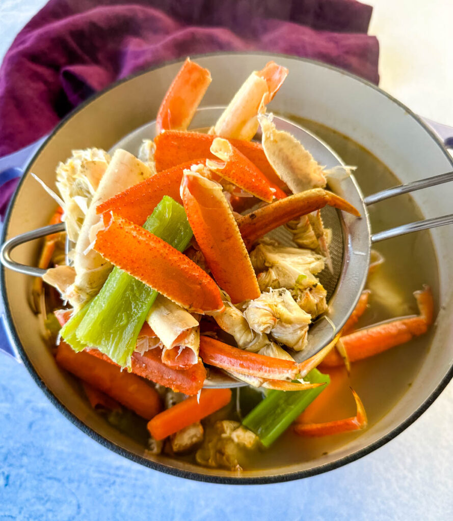strained homemade seafood stock with crab shells, carrots, and celery in a Dutch oven