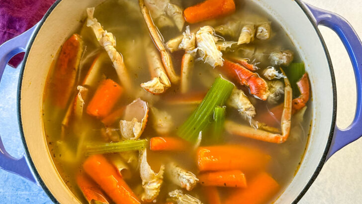 homemade seafood stock with crab shells, carrots, and celery in a Dutch oven